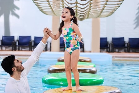 A girl balances on a lily pad float in indoor pool