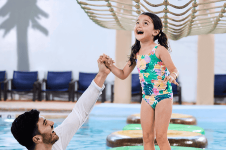 A girl balances on a lily pad float in indoor pool