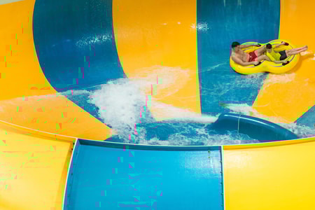 A father and son going down the Coyote Cannon water slide together on a yellow raft.