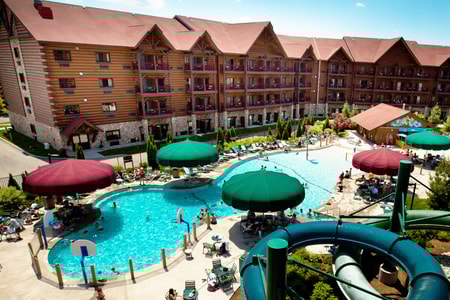 Aerial view of outdoor pool area featuring water slides, shaded seating under colorful umbrellas, and guests enjoying a sunny day.