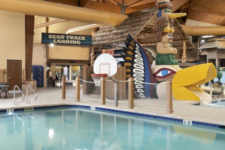 Indoor pool featuring a water slide and a basketball hoop for recreational activities.