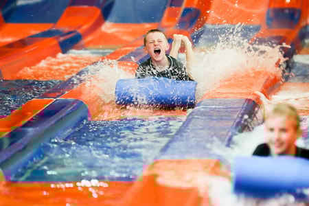 Two kids race down a waterslide laying on a blue mat