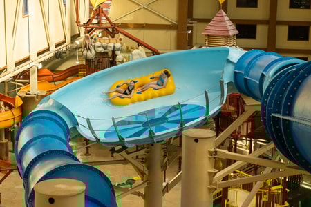 Two teenagers riding a yellow raft in an indoor water park