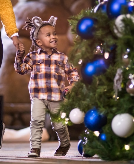 A kid and his mom walking past a holiday tree