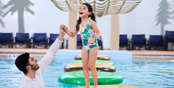 A girl balances on a lily pad float in indoor pool