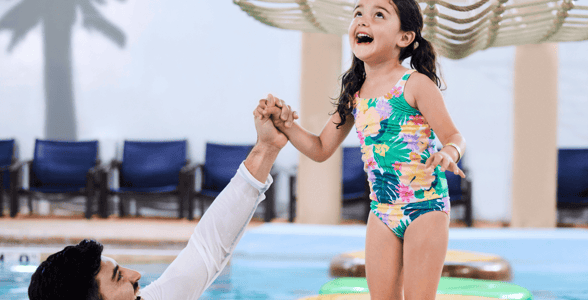 A girl balances on a lily pad float in indoor pool