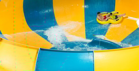 A father and son going down the Coyote Cannon water slide together on a yellow raft.