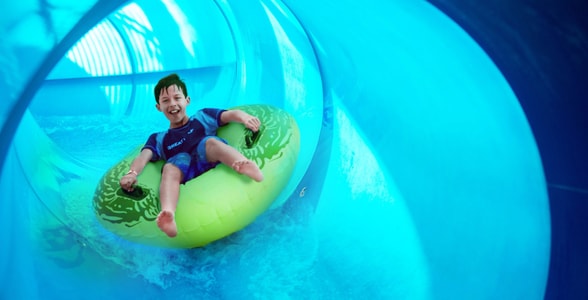 Boy rides down blue waterslide on yellow tube 