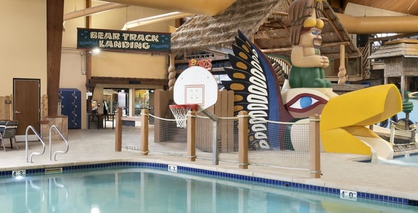 Indoor pool featuring a water slide and a basketball hoop for recreational activities.