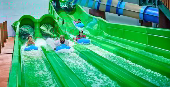 Guests race down a waterslide laying on a blue mat