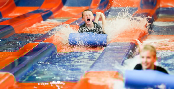 Two kids race down a waterslide laying on a blue mat