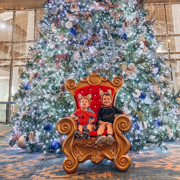 two kids seating in front of a big Christmas tree