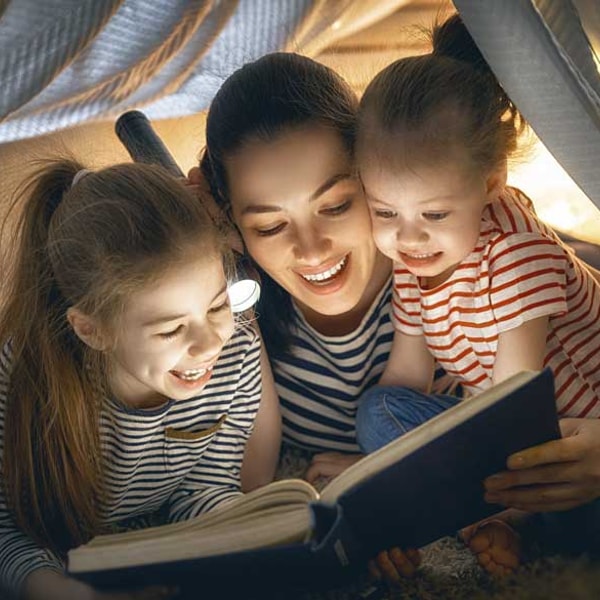 mom reading a book to her daughters under a tent