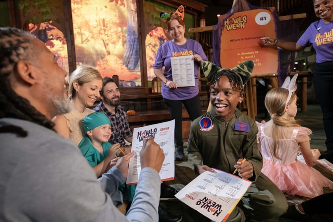 Families in Halloween costumes laugh while playing Howl-O-Ween trivia with Great Wolf Lodge staff