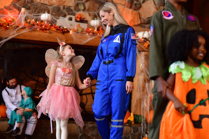 Child in fairy costume meeting astronaut character indoors.