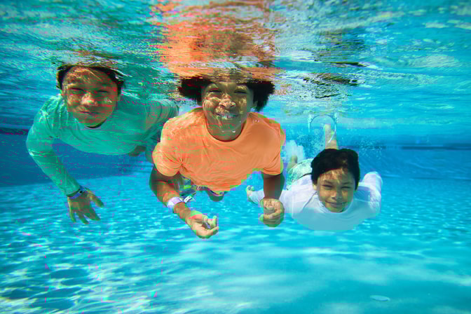 Three children smiling underwater in a swimming pool