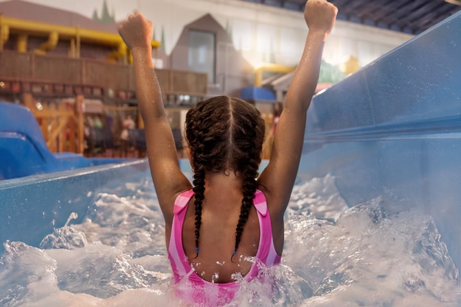 Child celebrating in water slide at indoor water park.