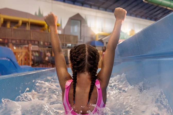 Child celebrating in water slide at indoor water park.