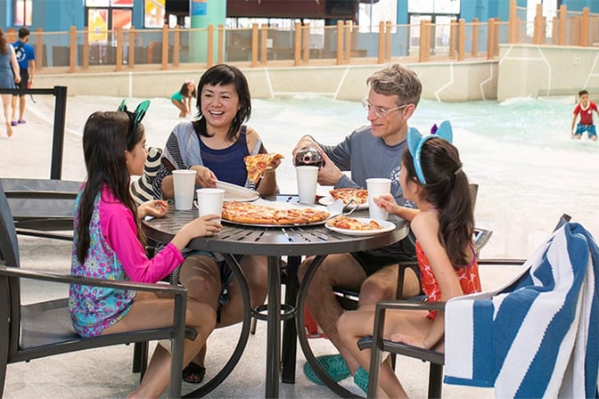 A family enjoy pizza and drinks in their own private seating at Great Wolf Lodge indoor water park and resort.