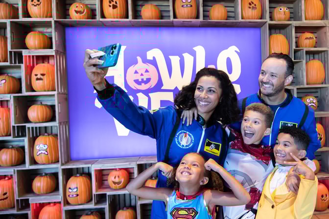 family of four taking a picture in front of a wall full of pumpkins