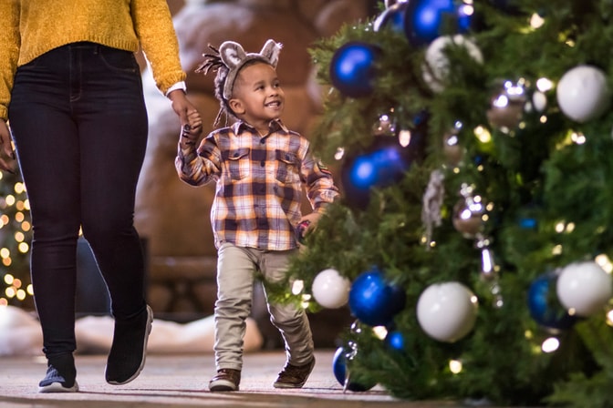 A kid and his mom walking past a holiday tree