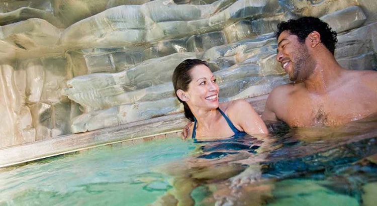 A couple relax in and on the side of the indoor pool 