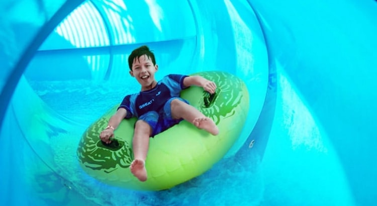 Boy rides down blue waterslide on green tube 
