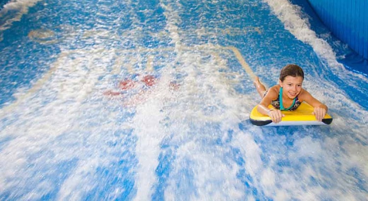 A child rides on a yellow boogie board in the water attraction 