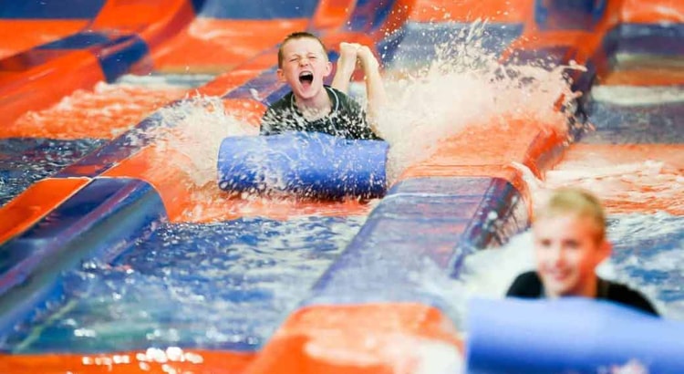 Two kids race down a waterslide laying on their stomaches 