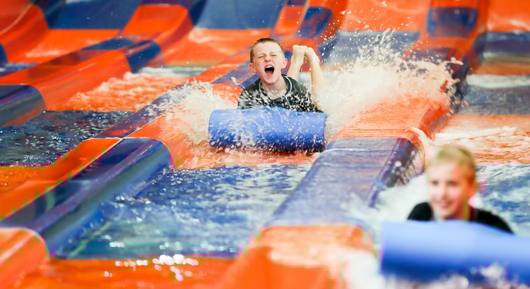 Two kids race down a waterslide laying on a blue mat