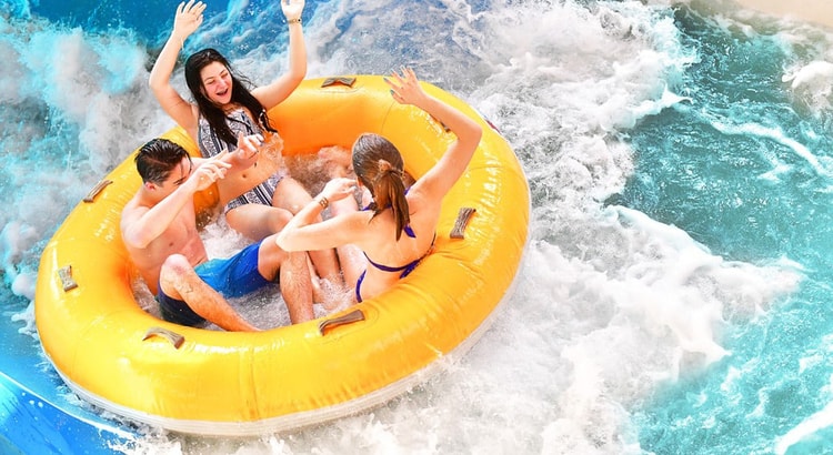 Three kids laugh as they ride in a yellow tube down a water slide