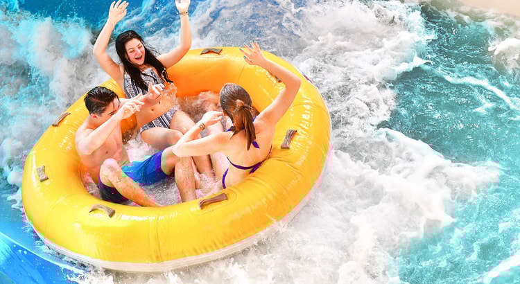 Three kids laugh as they ride in a yellow tube down a water slide