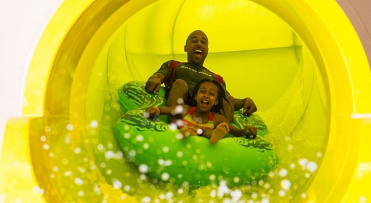 Dad and daughter ride down yellow waterslide in green tube