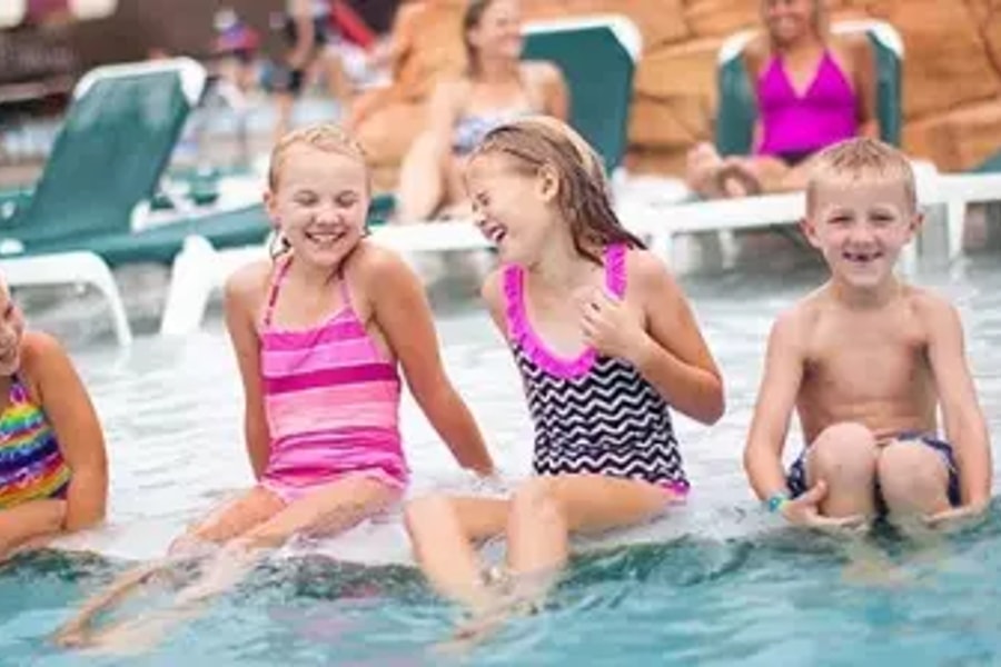 Four kids smile and laugh as they sit in a shallow outdoor pool 