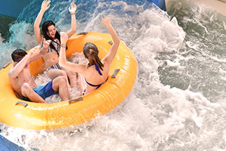 Three kids laugh as they ride in a yellow tube down a water slide