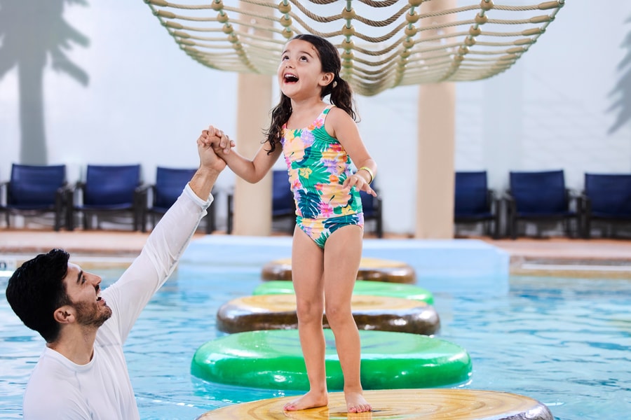 A girl balances on a lily pad float in indoor pool