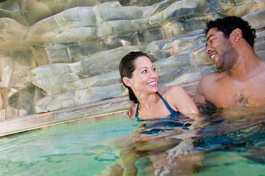 A couple relax in and on the side of the indoor pool 