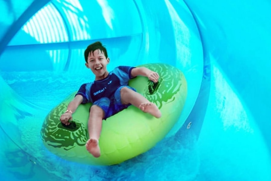 Boy rides down blue waterslide on green tube 