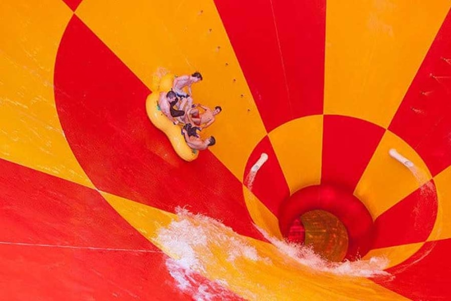 Four friends ride down a multicolored water slide in a tube 