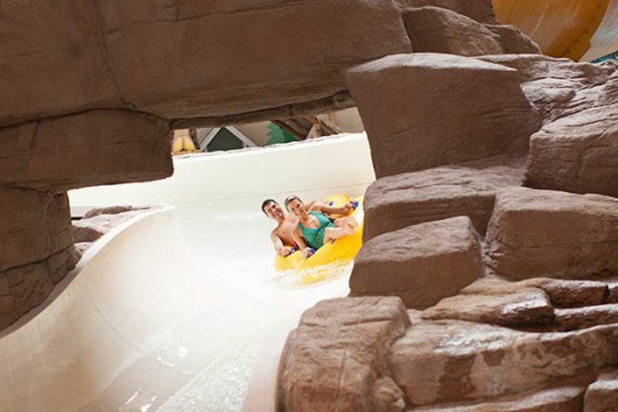A couple in a tube race down the water slide surrounded by rock decor