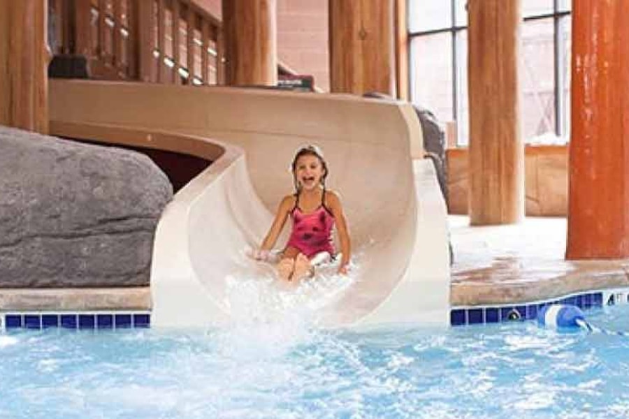 A girl laughs as she rides down a white water slide and a boy plays in the background
