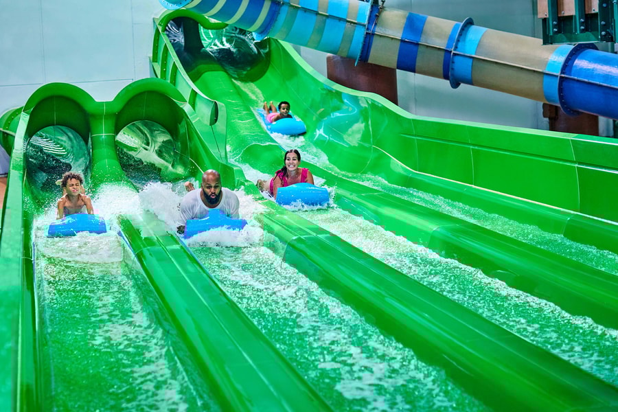 Guests race down a waterslide laying on a blue mat