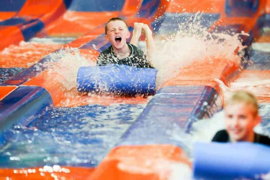 Two kids race down a waterslide laying on their stomaches 
