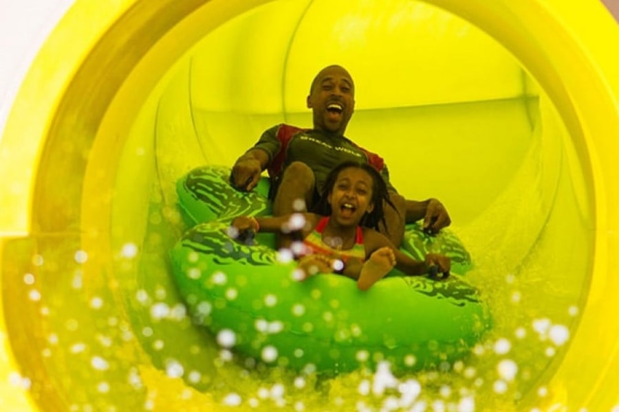 Dad and daughter ride down yellow waterslide in green tube