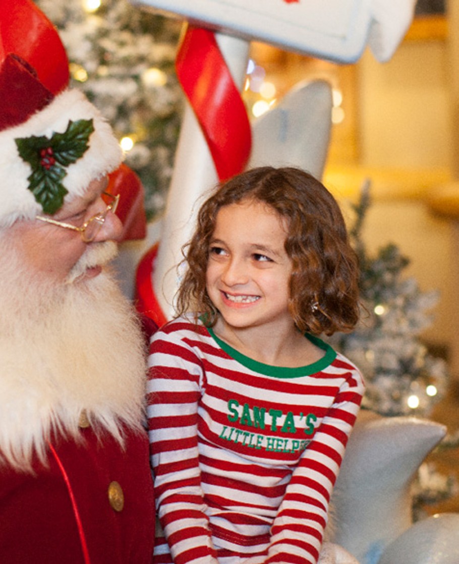 Little girl in holiday pajamas smiling at Santa