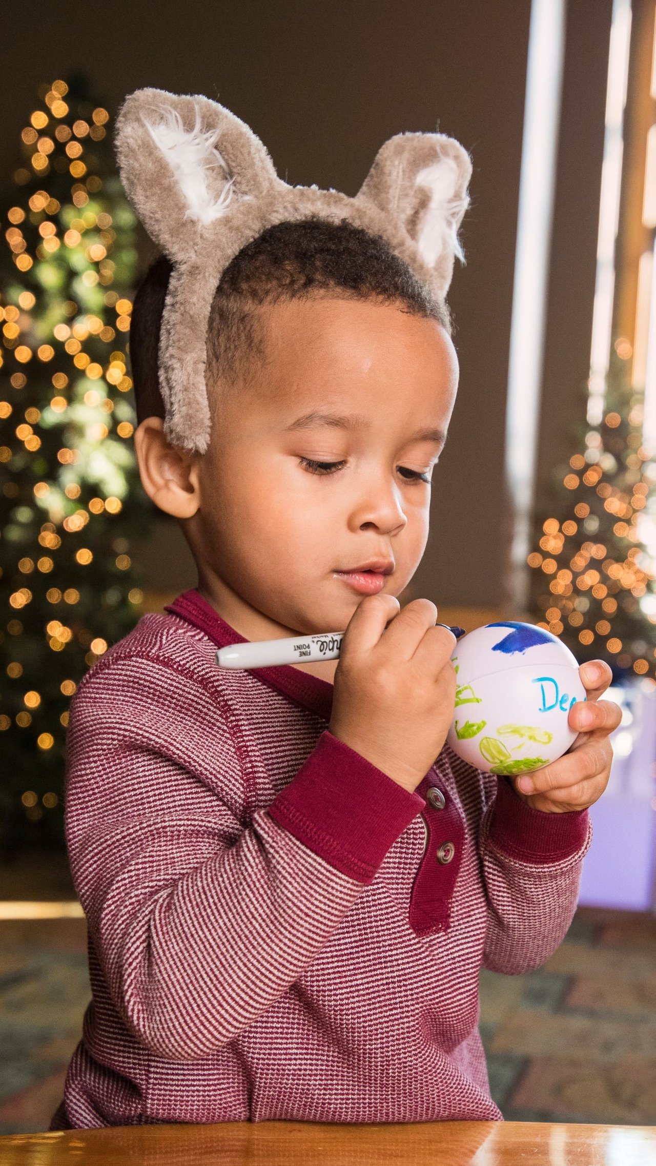 Child wearing fuzzy wolf ears decorating a holiday ornament