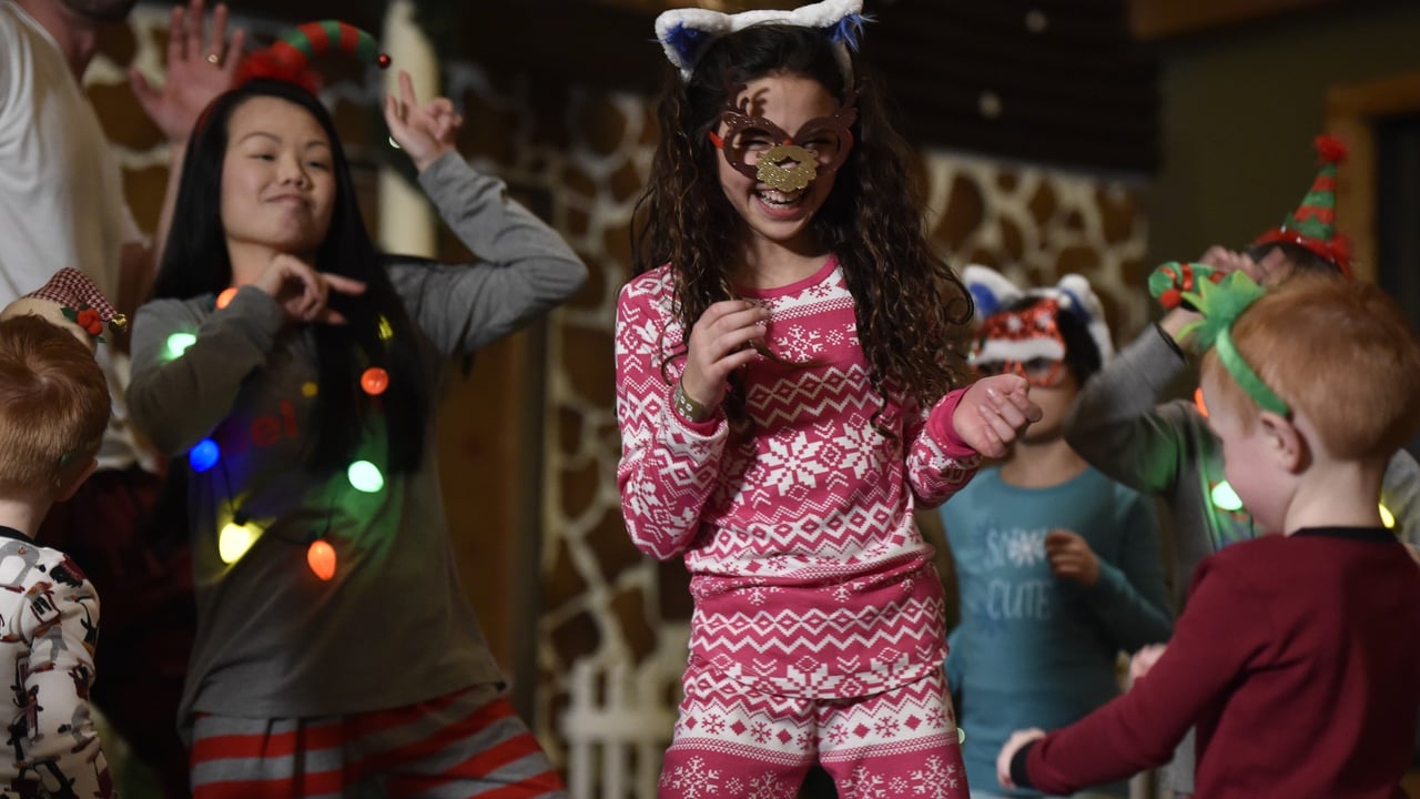 Kids in festive pajamas and reindeer masks dancing at a holiday celebration