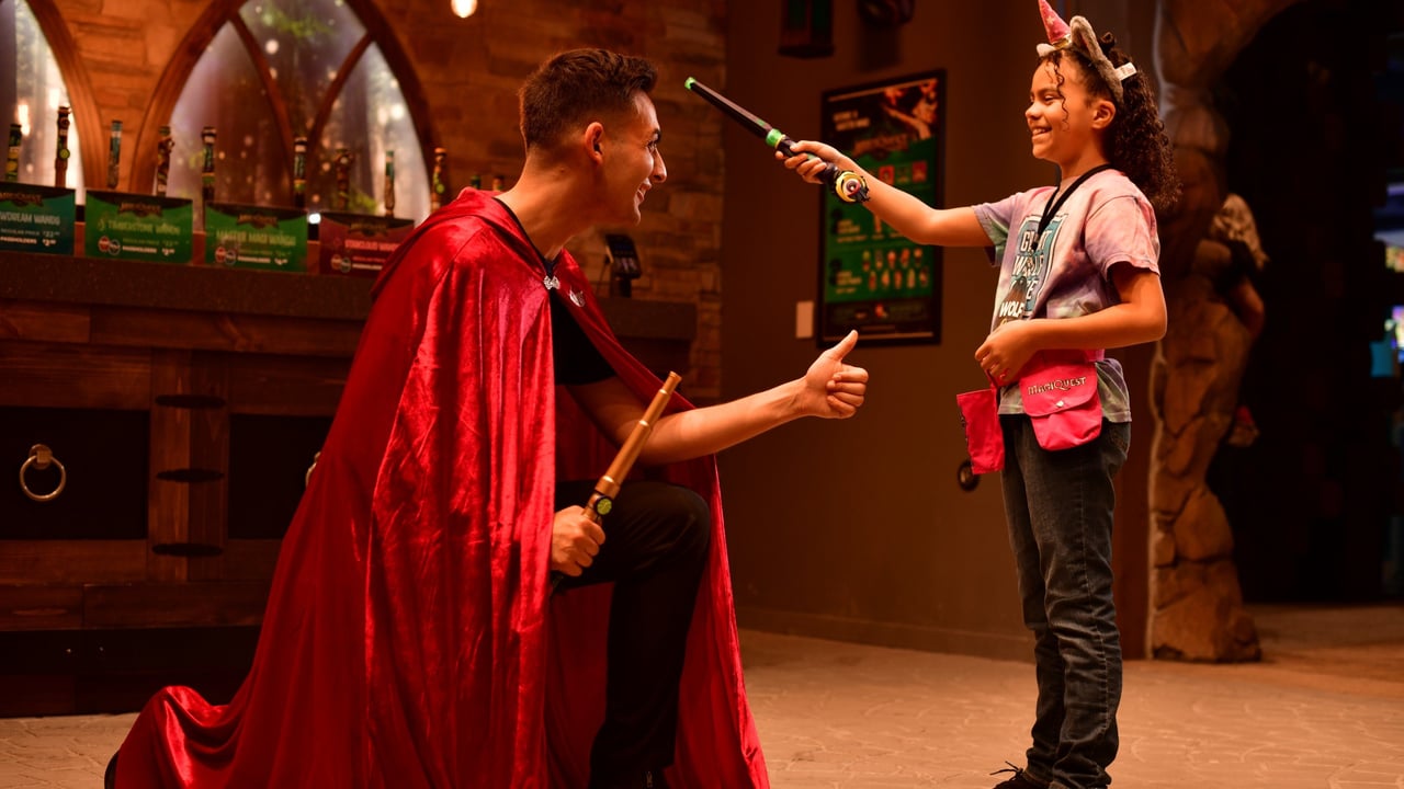 ChatGPT said: Girl smiling while pointing wand at kneeling man in cape