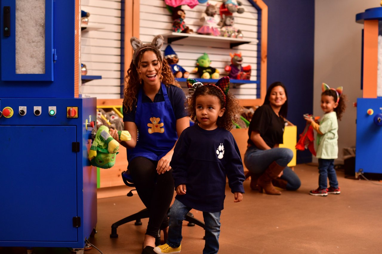 mothers and 2 girls watch as staff member stuffs a toy bear