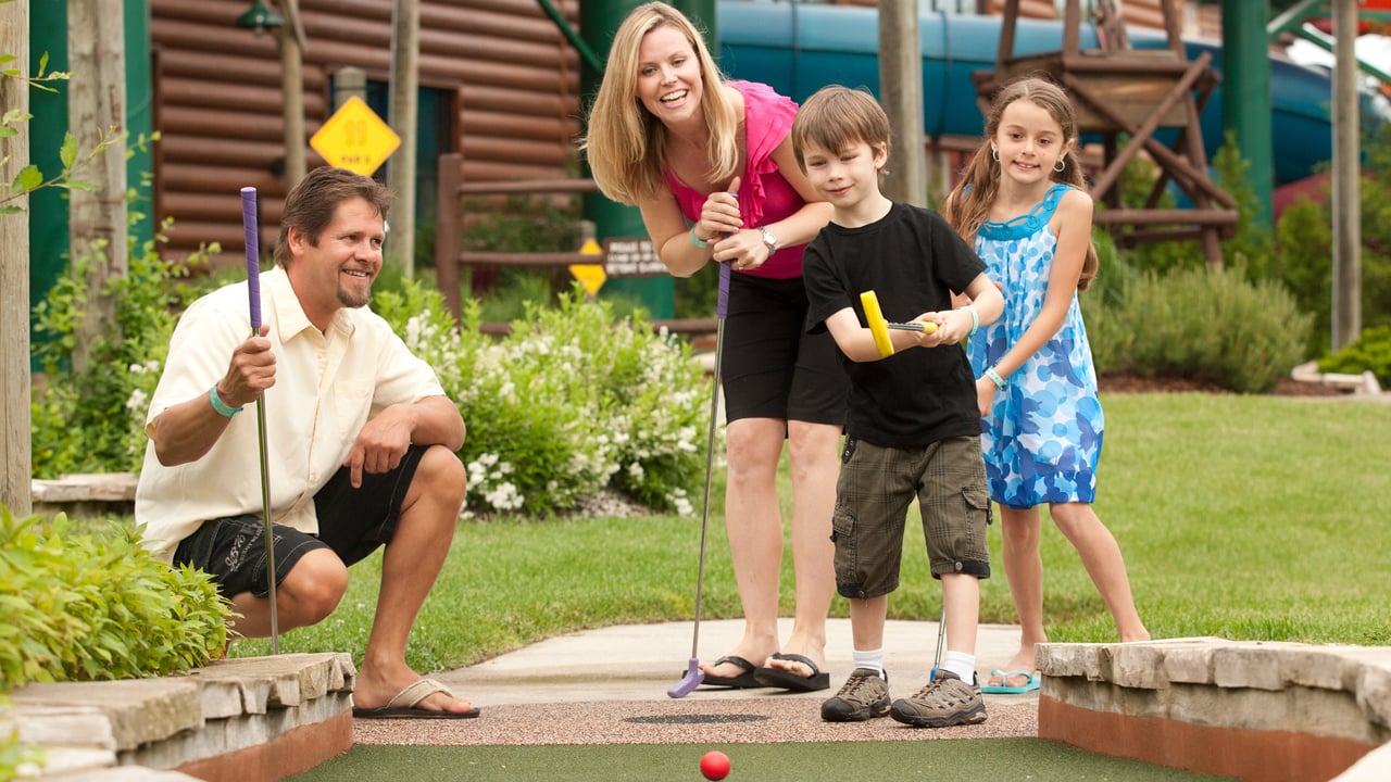 Upward angle looking toward a family after young girl putted, the pink ball is in frame as it rolls to the hole